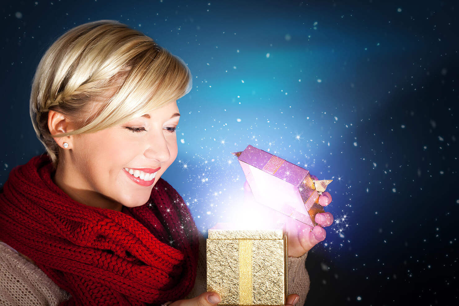 Lächelnde Frau in rotem Schal hält eine leuchtende Geschenkbox in winterlicher Atmosphäre.