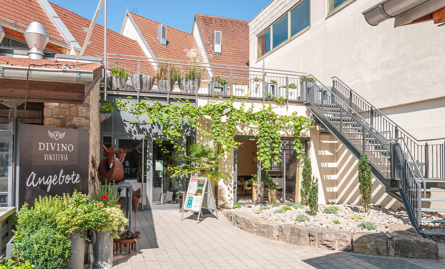 Grüne, begrünte Außenfassade der Divino-Vinoteria mit Treppe und Schildern.