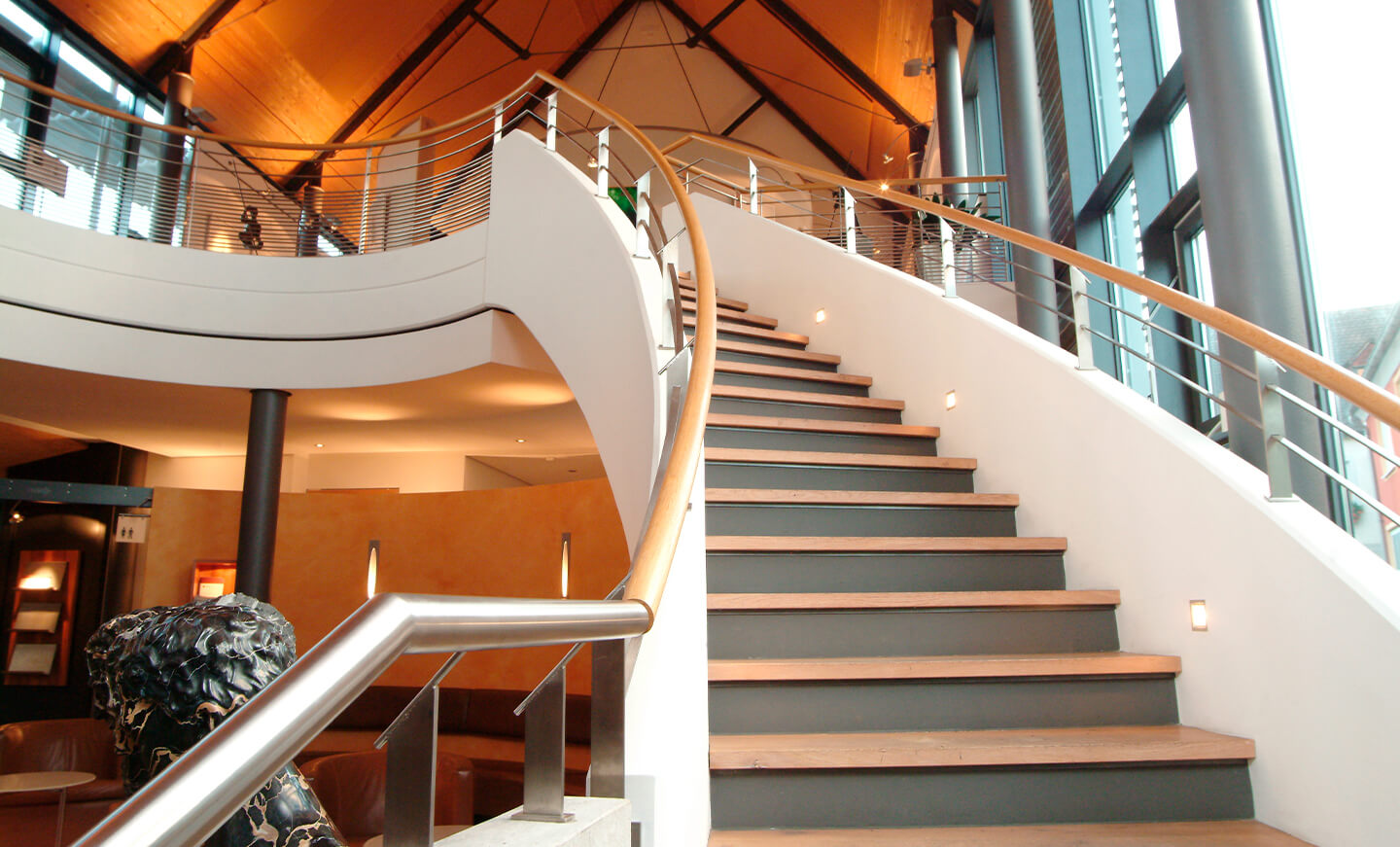 Geschwungene Treppe mit Galerie in lichtdurchflutetem Innenraum der Vinothek.